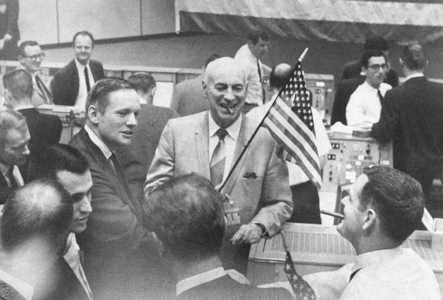 A big flag hangs in Mission Control at Manned Spacecraft Center in Houston, Tex., Dec. 27, 1968 after the completion of Apollo 8 spaceflight. Dr. Robert R. Gilruth, director of MSC holds a small flag while Astronaut Neil A. Armstrong, left, commander of Apollo 8 backup crew, congratulates Glynn S. Lunney, (white shirt) flight controller. Others are unidentified. (AP Photo) ORG XMIT: APHS362130