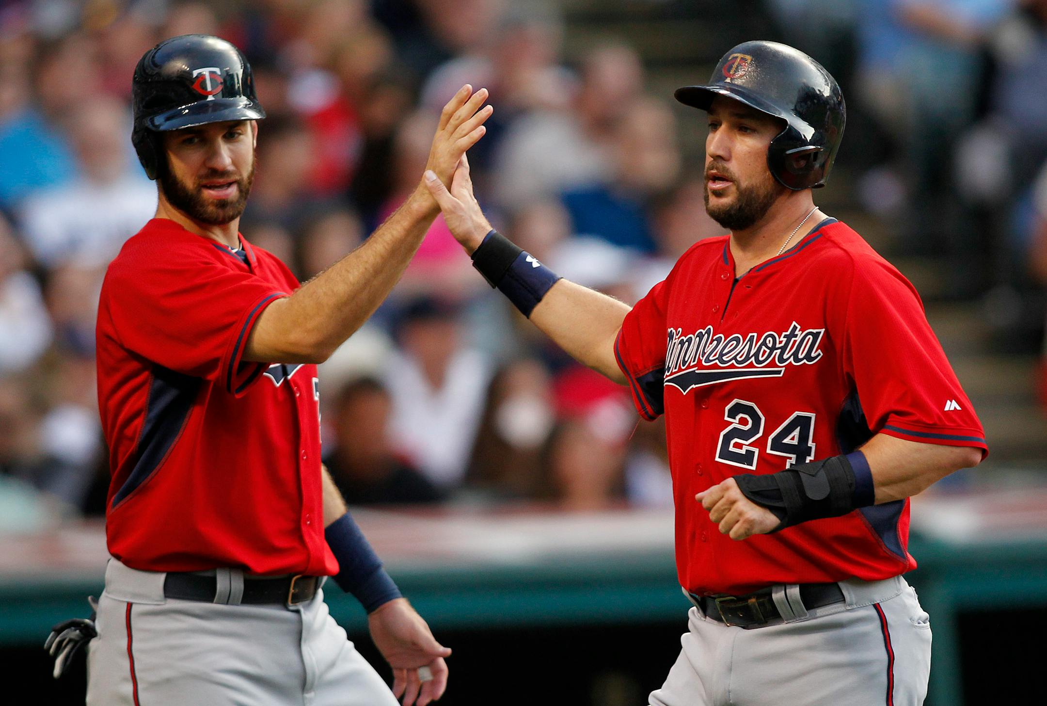 Minnesota Twins' Trevor Plouffe (24) is congratulated by teammate Joe Mauer after scoring on a single by Tori Hunter during the third inning of a baseball game against the Cleveland Indians, Friday, Aug. 7, 2015, in Cleveland. (AP Photo/Aaron Josefczyk)