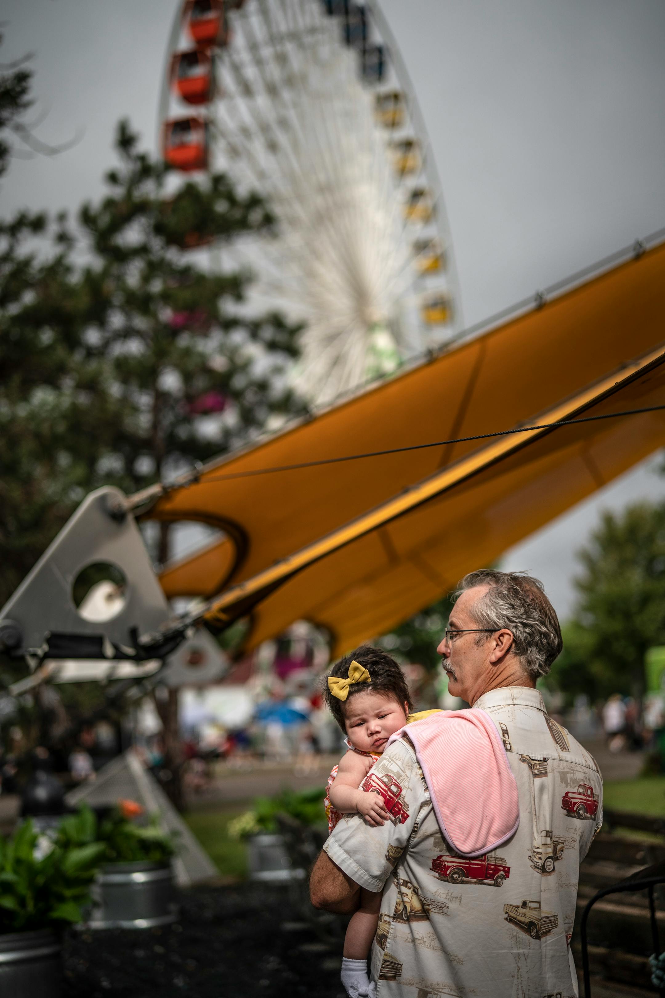 Mark Burgess held his 4 1⁄2-month-old great-niece Aurora DeBose as he attended a Mass at Baldwin Park on the Minnesota State Fairgrounds. The Mass was hosted by Corpus Christi Catholic Church of Roseville.