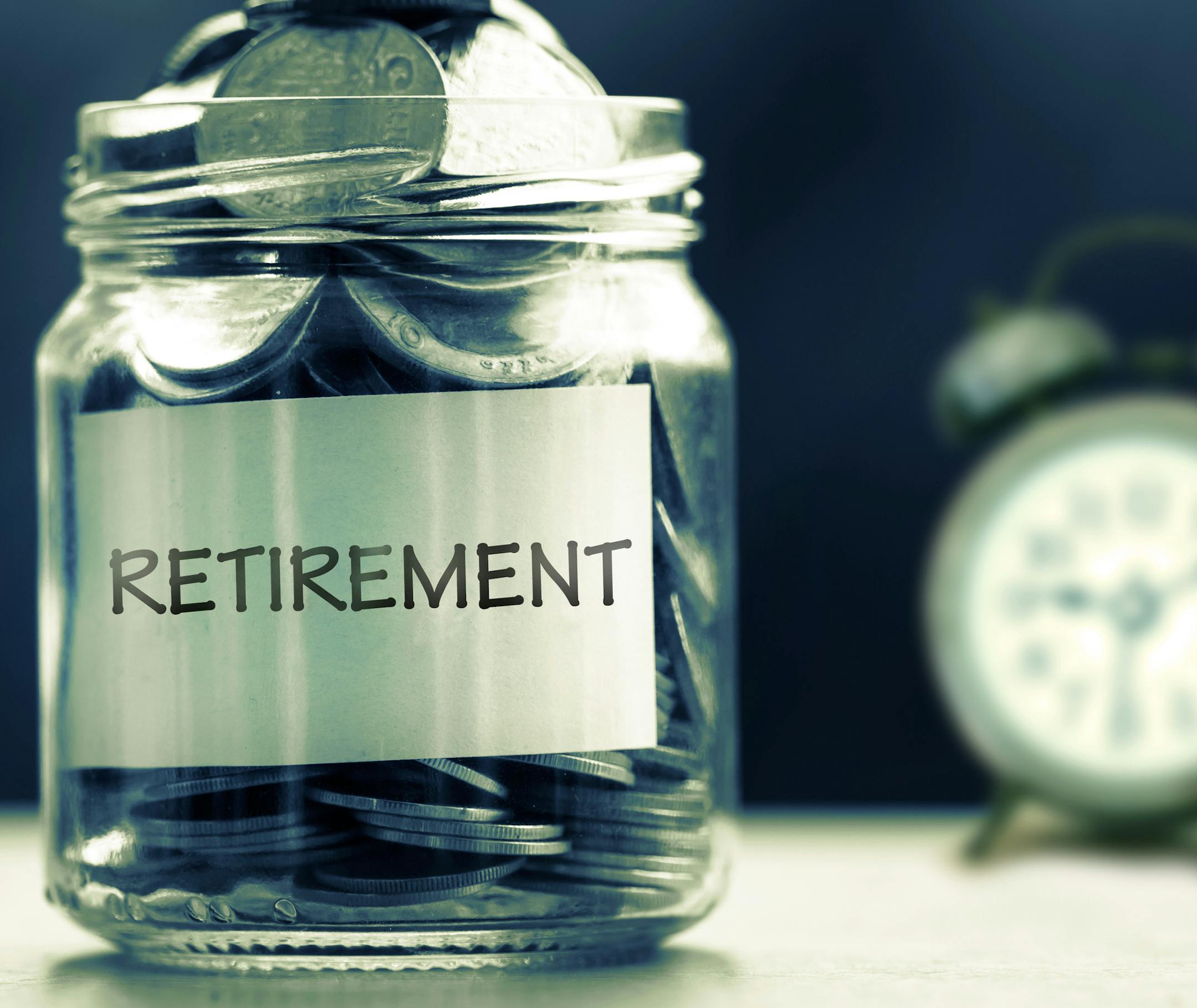 Close up Coins in glass jar with alarm clock for time to money saving for retirement concept , dark retro color tone