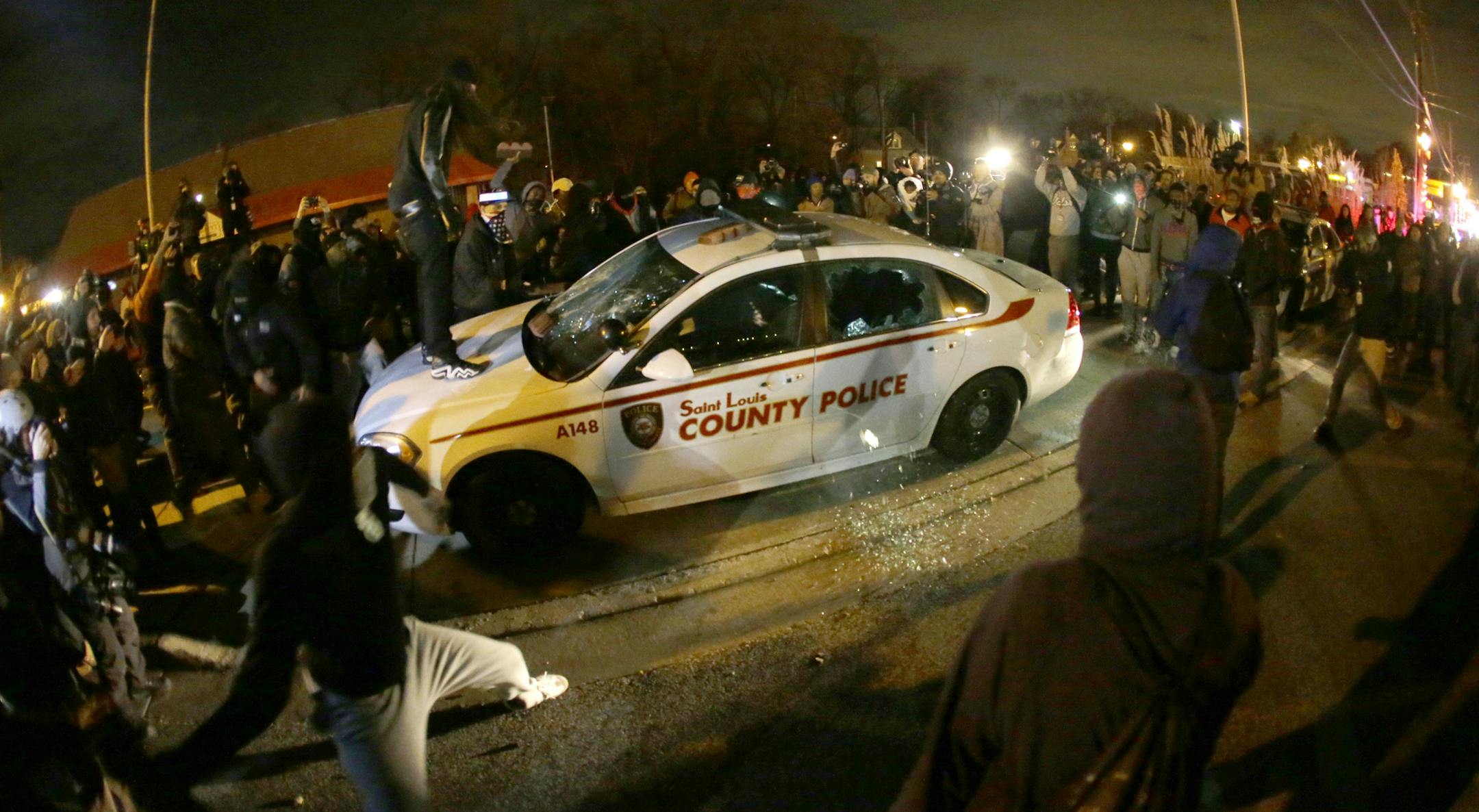 FOR USE AS DESIRED, YEAR END PHOTOS - FILE - A protester squirts lighter fluid on the police car as the car windows are shattered near the Ferguson Police Department after the announcement of the grand jury decision Monday, Nov. 24, 2014, in Ferguson, Mo. A grand jury has decided not to indict Ferguson police officer Darren Wilson in the death of Michael Brown, the unarmed, black 18-year-old whose fatal shooting sparked sometimes violent protests. (AP Photo/Charlie Riedel, File)