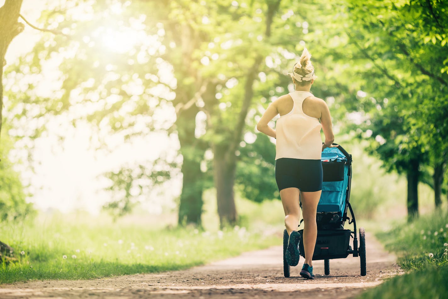 Running woman with baby stroller enjoying summer day in park. Jogging or power walking supermom, active family with baby jogger.