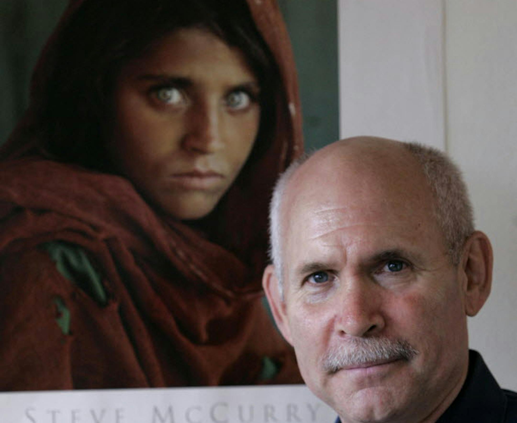 FILE -- Photographer Steve McCurry poses for a portrait in New York in September 2008 with a poster of his iconic photo of the Afghan girl, Sharbat Gulla, which became one of the most famous National Geographic covers.