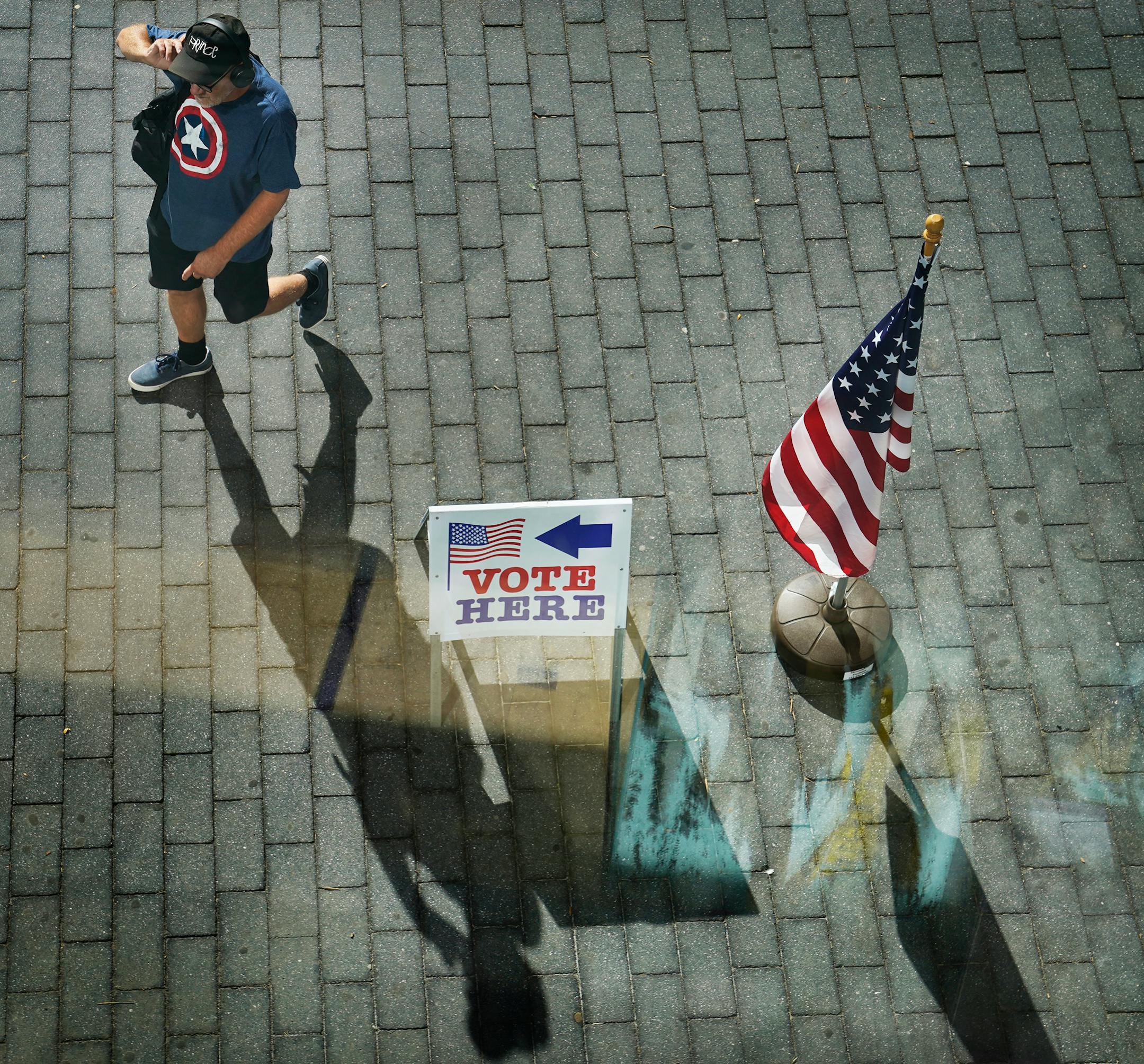 A man casts a shadow while walking by a voting sign at the Minneapolis Central Library during the primary election that includes the 5th congressional district in Minneapolis.