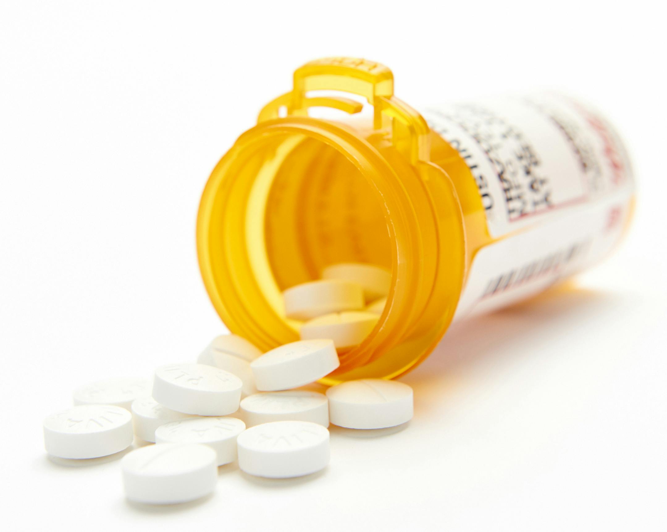 Pill bottle on its side with white round pills spilling out with shallow depth of field and a white backdrop