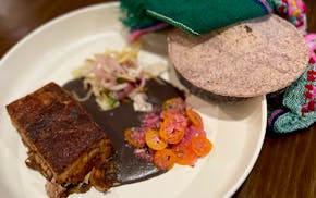 A whote plate with a rectangle of crispy-topped meat on a puddle of black bean puree, and a pile of thin slices of orange kumquats