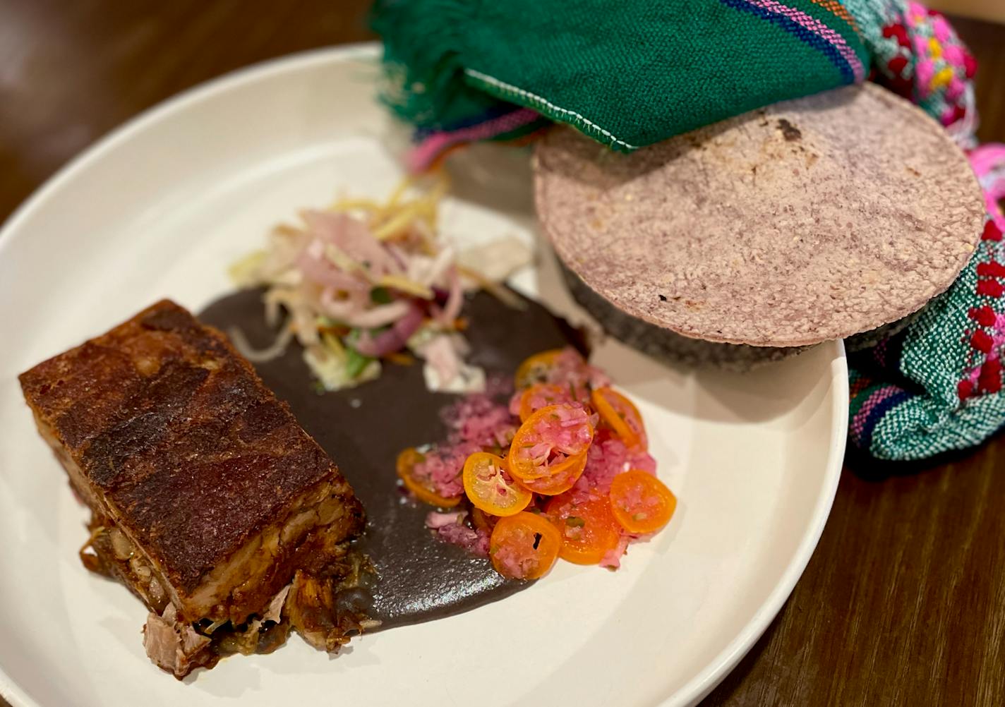 A whote plate with a rectangle of crispy-topped meat on a puddle of black bean puree, and a pile of thin slices of orange kumquats