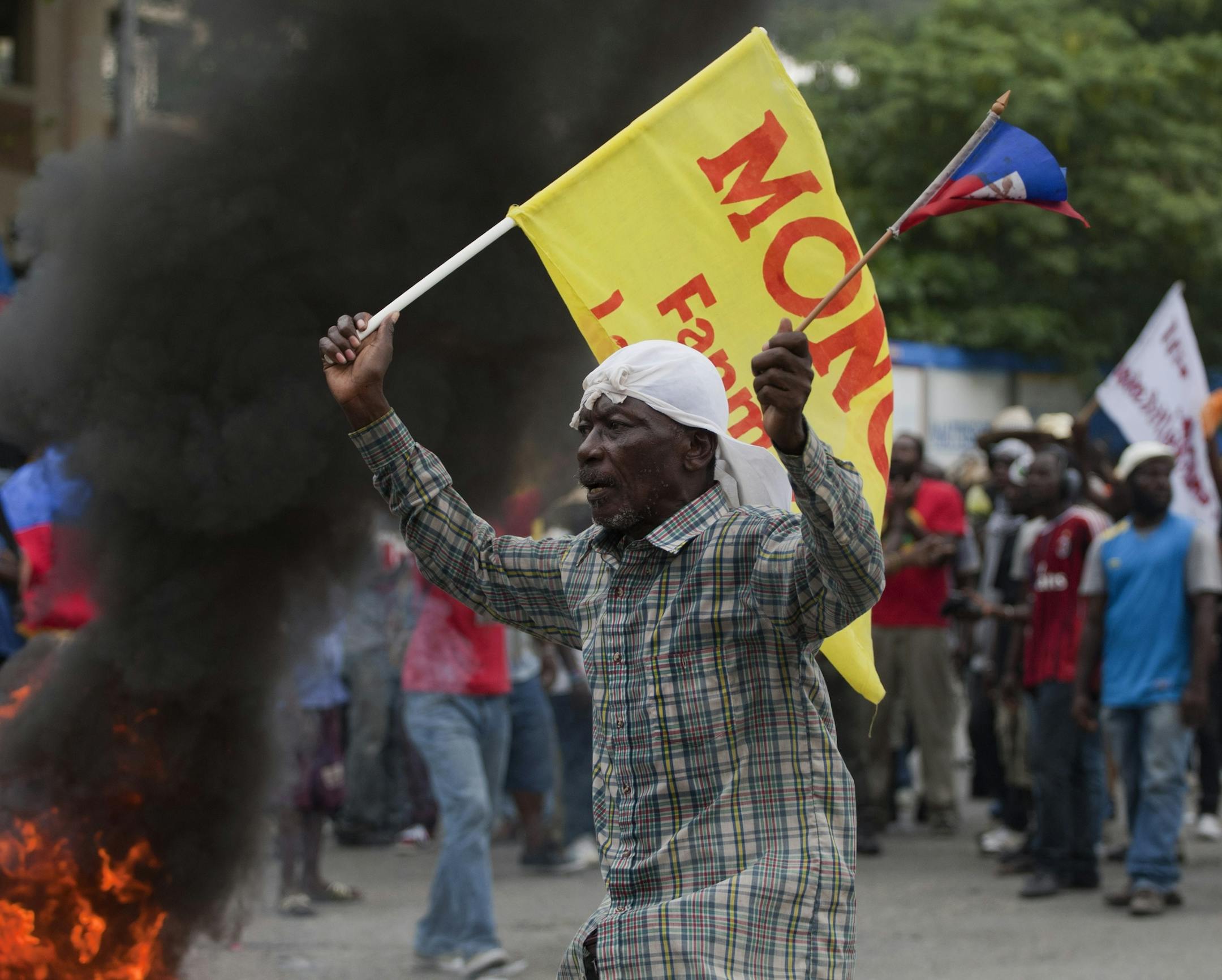 An anti-government demonstrator walks with a political party flag, in the street, during a protest calling for the resignation of Haiti's President Michel Martelly in Port-au-Prince, Haiti, Tuesday, Dec. 16, 2014. Haiti's capital has endured a growing number of demonstrations in recent weeks during which protesters have demanded the holding of elections that were expected in 2011 and the resignations of Prime Minister Laurent Lamothe as well as President Michel Martelly. Lamothe resigned over th
