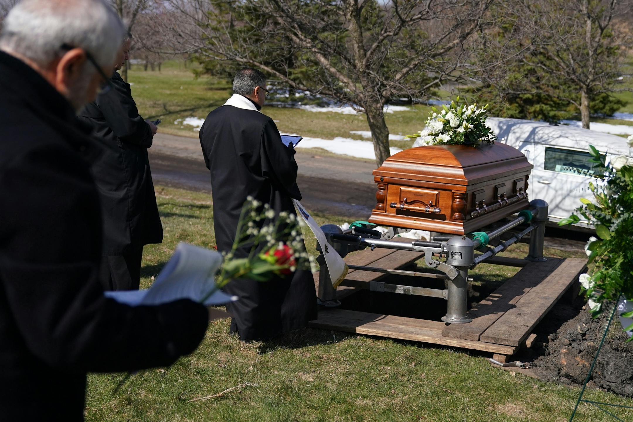 Chorbishop Sharbel Maroun, center, spread incense over the casket of Elie Farhat, who recently died of COVID-19 at the age of 92, as friends and family worked to keep the recommended distance from one another at his gravesite Thursday.