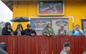 People watch in the rain as some protested law enforcement outside Las Cuatro Milpas restaurant during a federal raid in Minneapolis on Tuesday, June