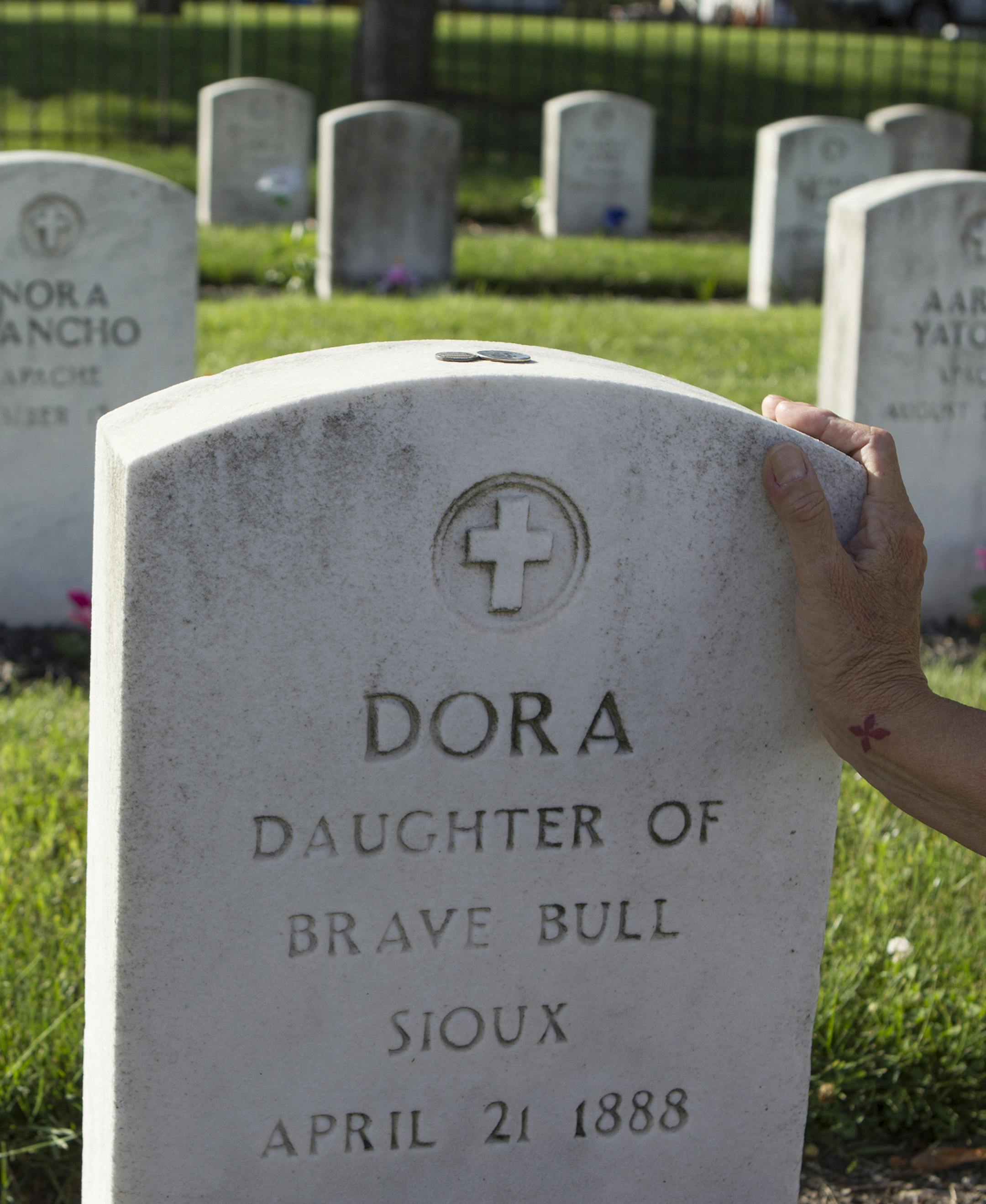 A woman places her hand on the gravestone of Dora Brave Bull at the Indian Cemetery at the Carlisle Barracks in July, 2014. Dora, a Rosebud Sioux, was among the first group of students to arrive at the school on Oct. 6, 1879. She passed away on April 24, 1881. The Rosebud Sioux in South Dakota have begun efforts to repatriate the remains of the 10 Rosebud students buried on the Carlisle school grounds. (Charles Fox/Philadelphia Inquirer/TNS)