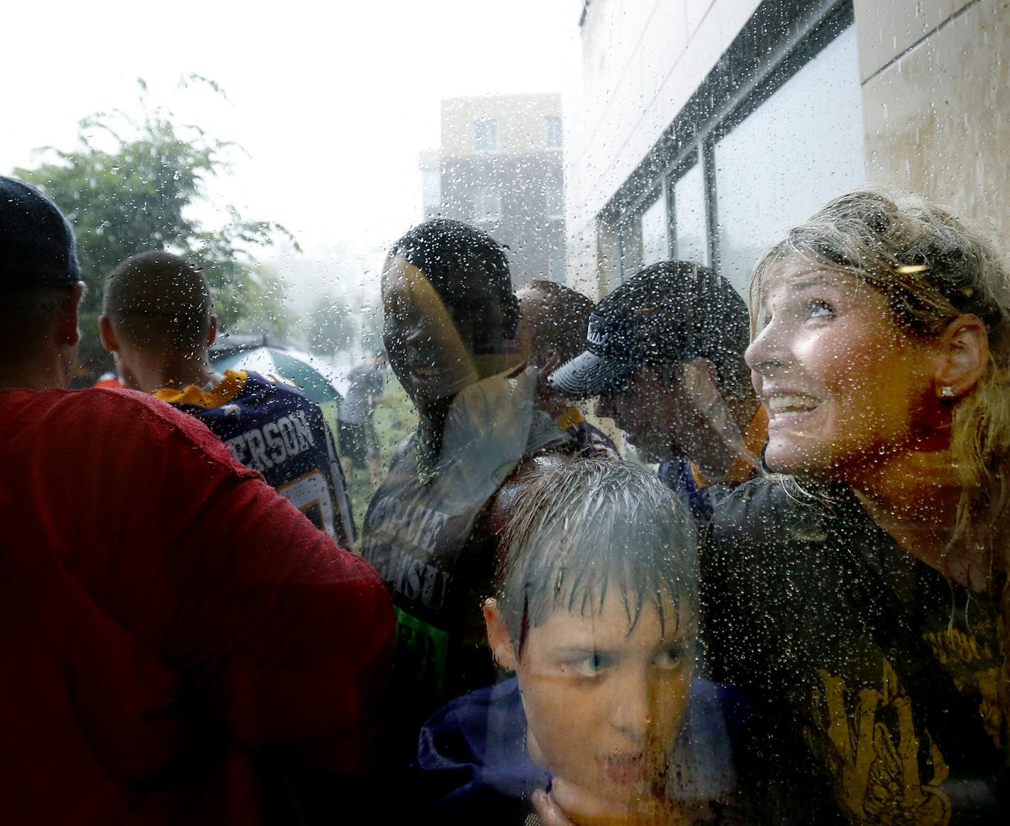 Minnesota Vikings fans Carter Phillips, 10, and his mother Janalyn of Waukee, Iowa sought cover by a window from the heavy rain during a storm while waiting for Vikings players to arrive at training camp at Minnesota State University, Mankato on Thursday. ] CARLOS GONZALEZ cgonzalez@startribune.com July 25, 2013, Minnesota Vikings Training Camp, Mankato, Minn., Minnesota State University, Mankato