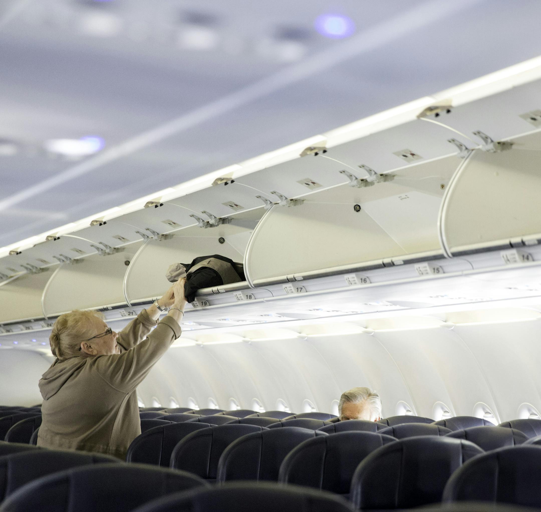 istock photo of a woman putting luggage into an overhead bin.