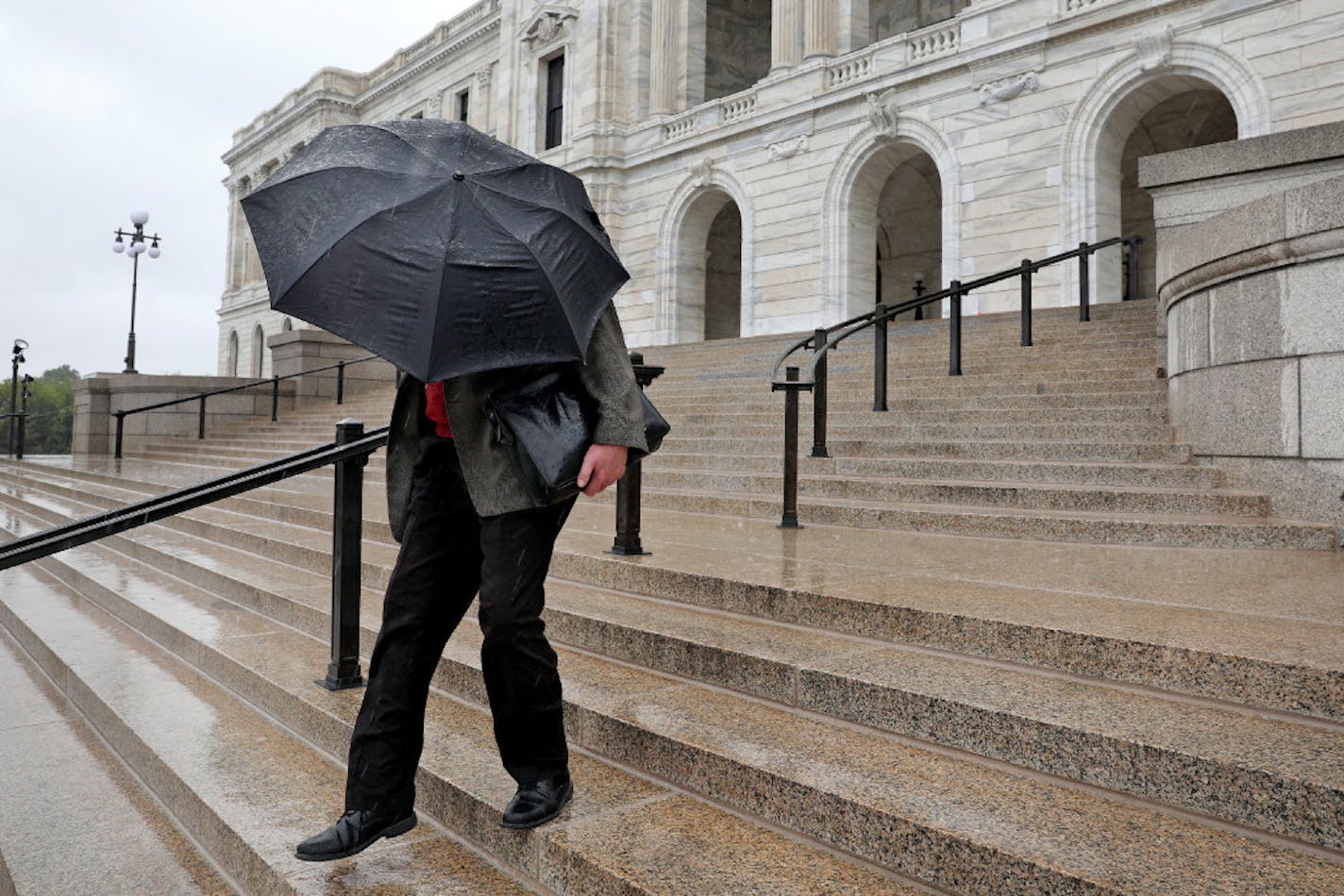 A man shielded himself from the rain with an umbrella as he walked down the steps of the State Capitol Saturday in St. Paul.