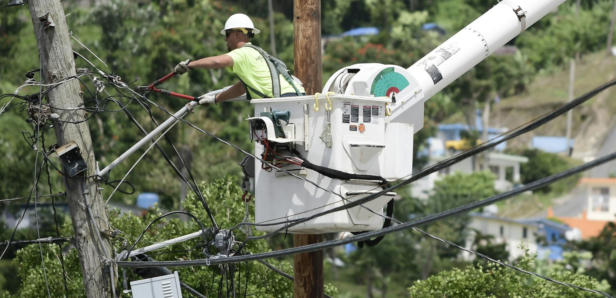In this May 16, 2018 photo, a worker from the Cobra Energy Company, contracted by the Army Corps of Engineers, installs power lines in the Barrio Martorel area of Yabucoa, a town where many residents continue without power in Puerto Rico. Trump administration officials say a big federal presence is no longer needed to hook up the relatively few remaining connections in the often-remote areas where people are still without power. (AP Photo/Carlos Giusti)