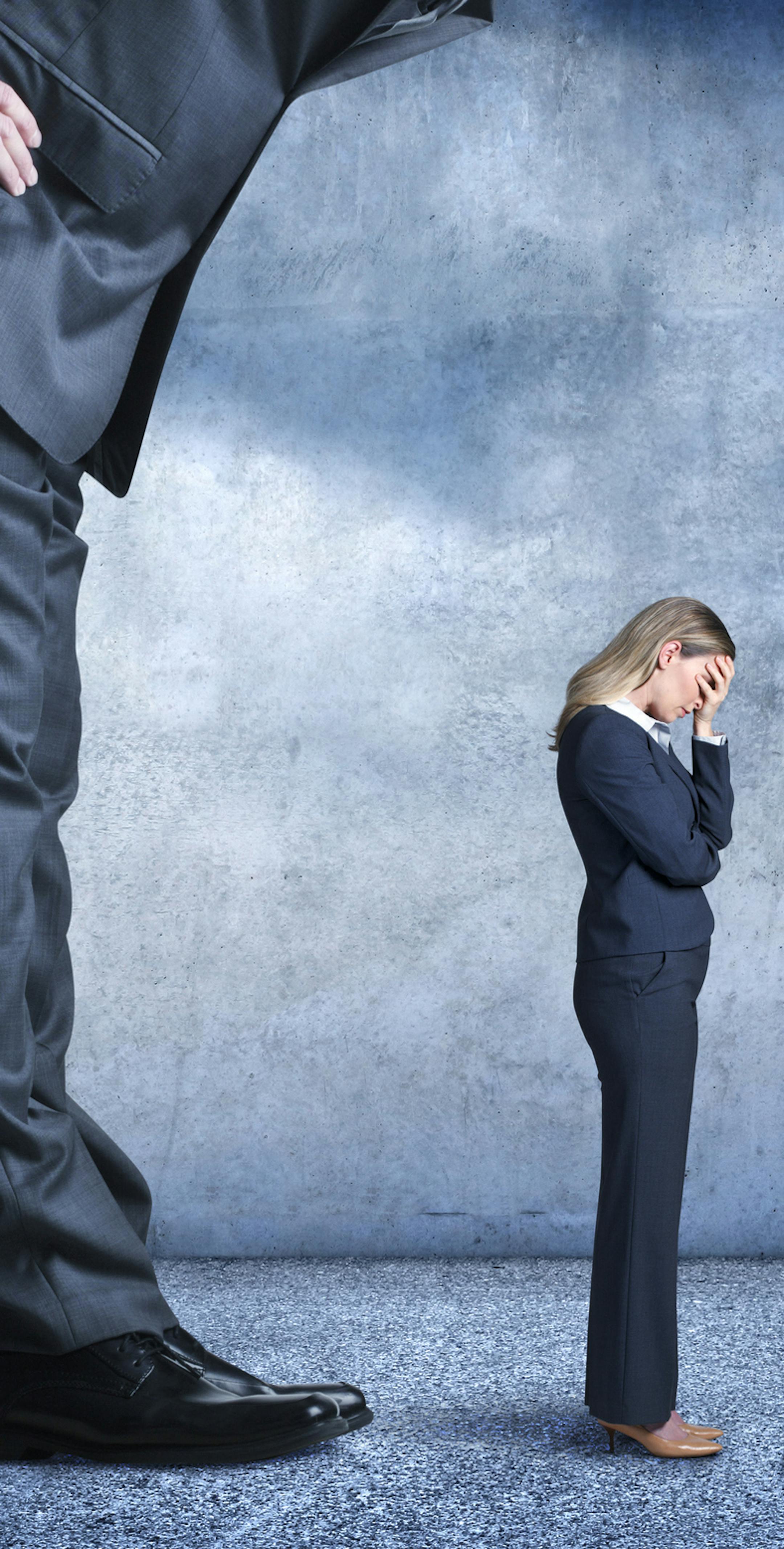 A businesswoman stands with her head buried in her hands as she tries to withstand the stress of gender or workplace discrimination from her much larger boss.