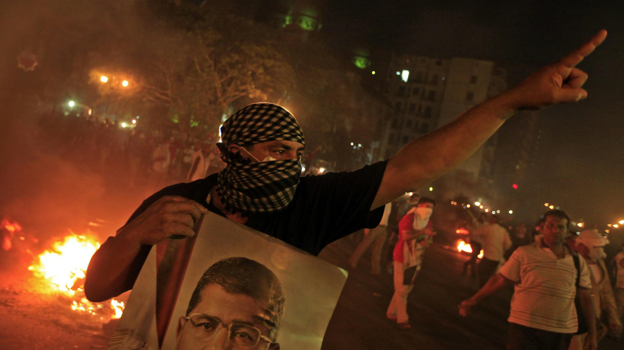 A Supporter of ousted President Mohammed Morsi holds a poster of him during clashes in downtown Cairo, Egypt, Monday, July 15, 2013. Thousands of supporters of deposed President Mohammed Morsi held mass rallies and marched in the streets Monday to demand his return to office. The protest turned violent in downtown Cairo as police fired tear gas at pro-Morsi protesters who burned tires, threw rocks and blocked traffic flow on a main roadway running through the heart of the capital. (AP Photo/Khal