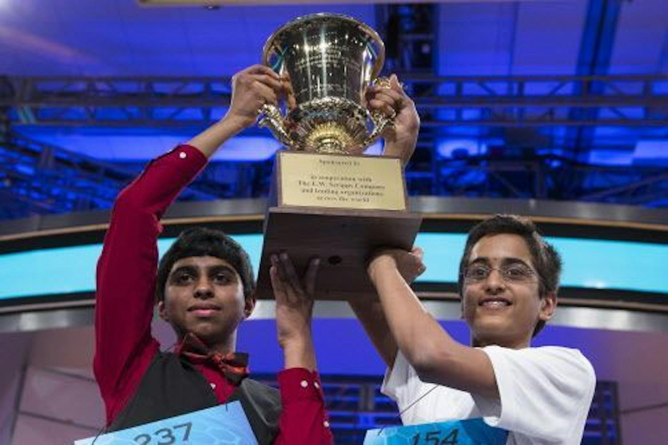 Ansun Sujoe, 13, left, of Fort Worth, Texas, and Sriram Hathwar, 14, of Painted Post, N.Y., raise the championship trophy after being named co-champions of the Scripps National Spelling Bee, on Thursday, May 29, 2014, in Oxon Hill, Md.