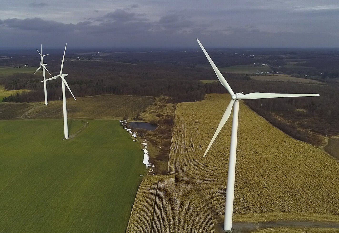 In this Nov. 25, 2019 photo, wind turbines slowly rotate over corn fields in Warsaw, N.Y. Renewable energy groups are pushing New York to help meet its ambitious climate change goals by charging electric generators for the carbon pollution they create. Putting a price on carbon will help New York meets its aggressive goal of 70% of its electricity coming from wind, solar and other renewable sources by 2030, the Alliance for Clean Energy New York said in a report. (AP Photo/Julie Jacobson)