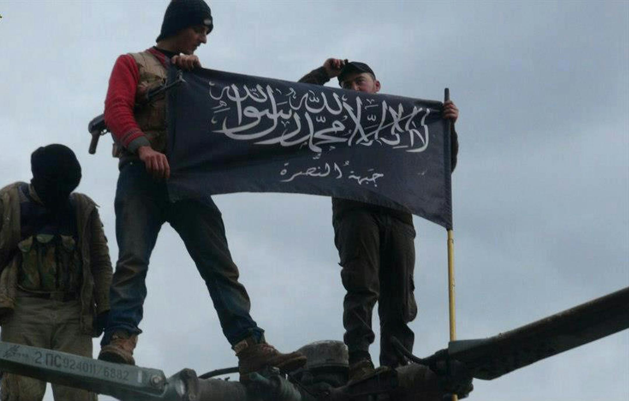 FILE - This Friday, Jan. 11, 2013 file citizen journalism image provided by Edlib News Network, ENN, which has been authenticated based on its contents and other AP reporting, shows rebels from al-Qaida affiliated Jabhat al-Nusra waving their brigade flag as they stand on a Syrian air force helicopter, at Taftanaz air base that was captured by the rebels, in Idlib province, northern Syria. Arabic on the flag reads, "There is no God but Allah and Mohammed is his prophet, Jabhat al-Nusra." On Syri