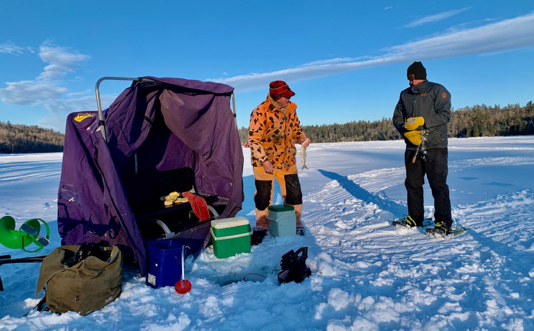 Pete Harris, left, and Terry Arnesen fishing for lake trout, a sample of which Harris holds in his bare hand.