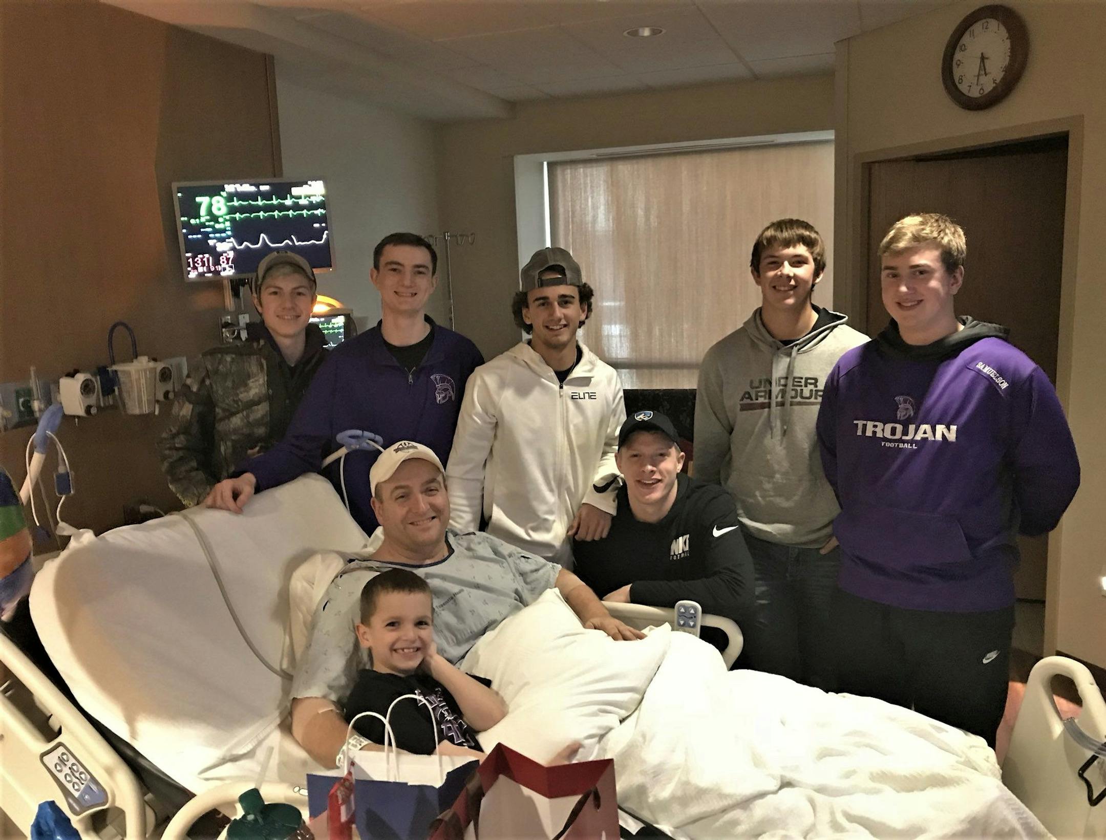 Barnesville coach Bryan Strand in his hospital bed after his stroke last March. With him is his son and a number of his football players.