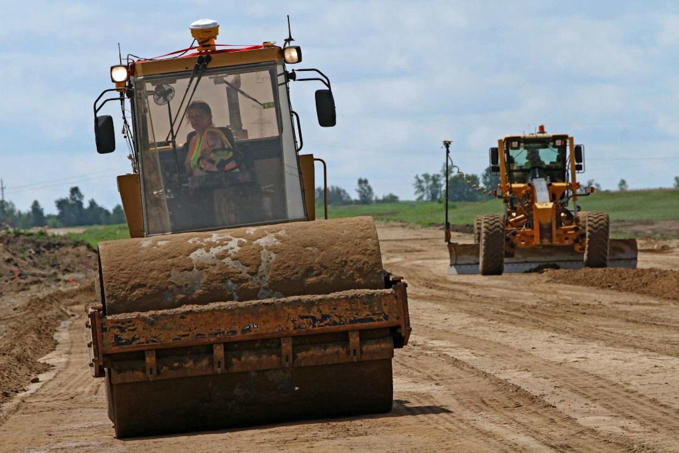 Driver Becky Radle, left, ran a roller on the Hwy. 23 bypass project near Paynesville, Minn., as work crews tried to get the back on track after the state shutdown and bad weather.