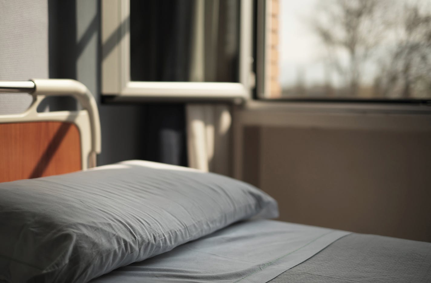 Hospital bed in soft window light. Focus, shallow, on bed only.