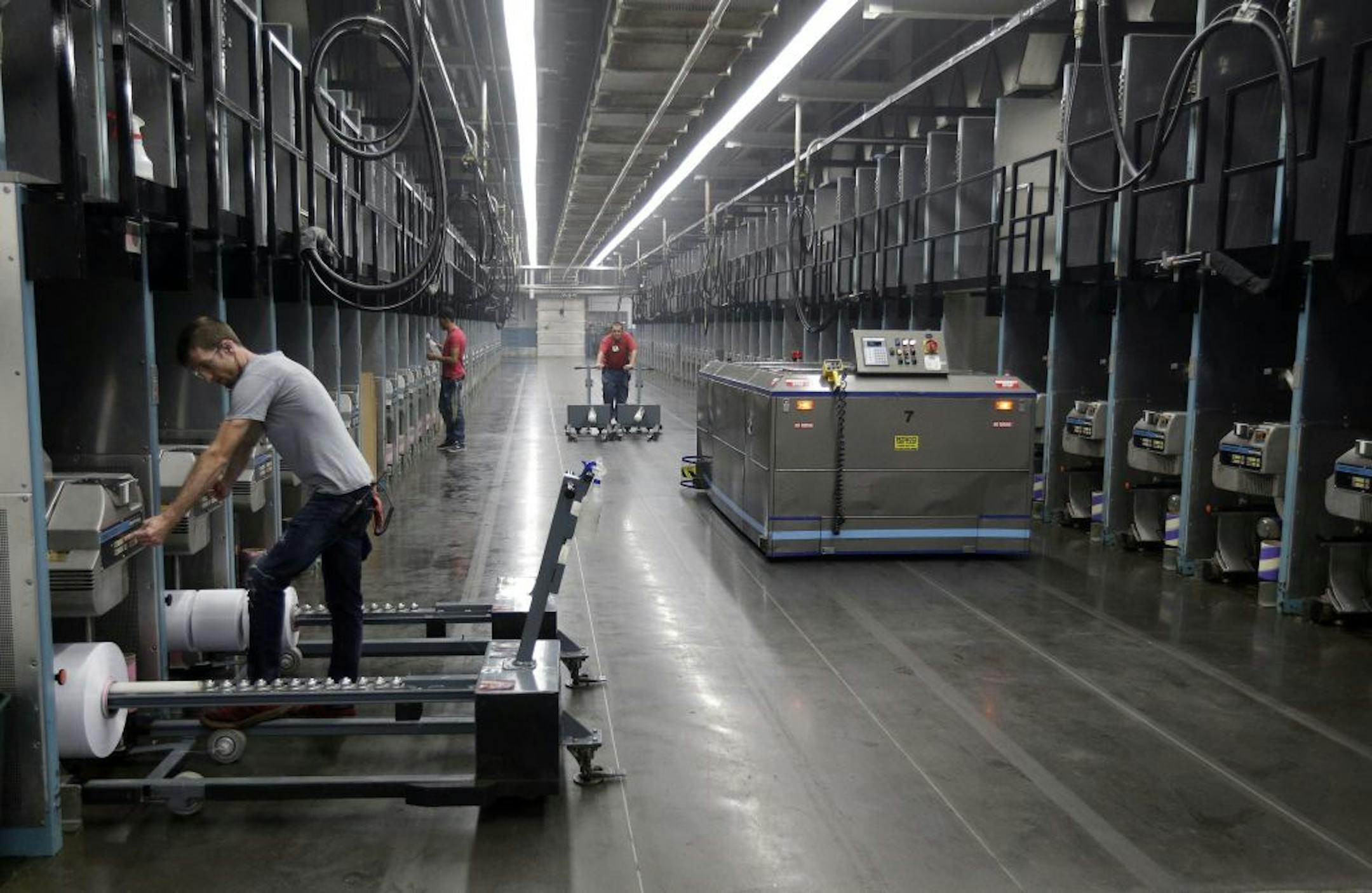 Workers exchange spools of thread as a robot picks up thread made from recycled plastic bottles at the Repreve Bottle Processing Center, part of the Unifi textile company in Yadkinville, N.C., Friday, Oct. 21, 2016. America has lost more than 7 million factory jobs since manufacturing employment peaked in 1979. Yet American factory production, minus raw materials and some other costs, more than doubled over the same span to $1.91 trillion last year, according to the Commerce Department, which us