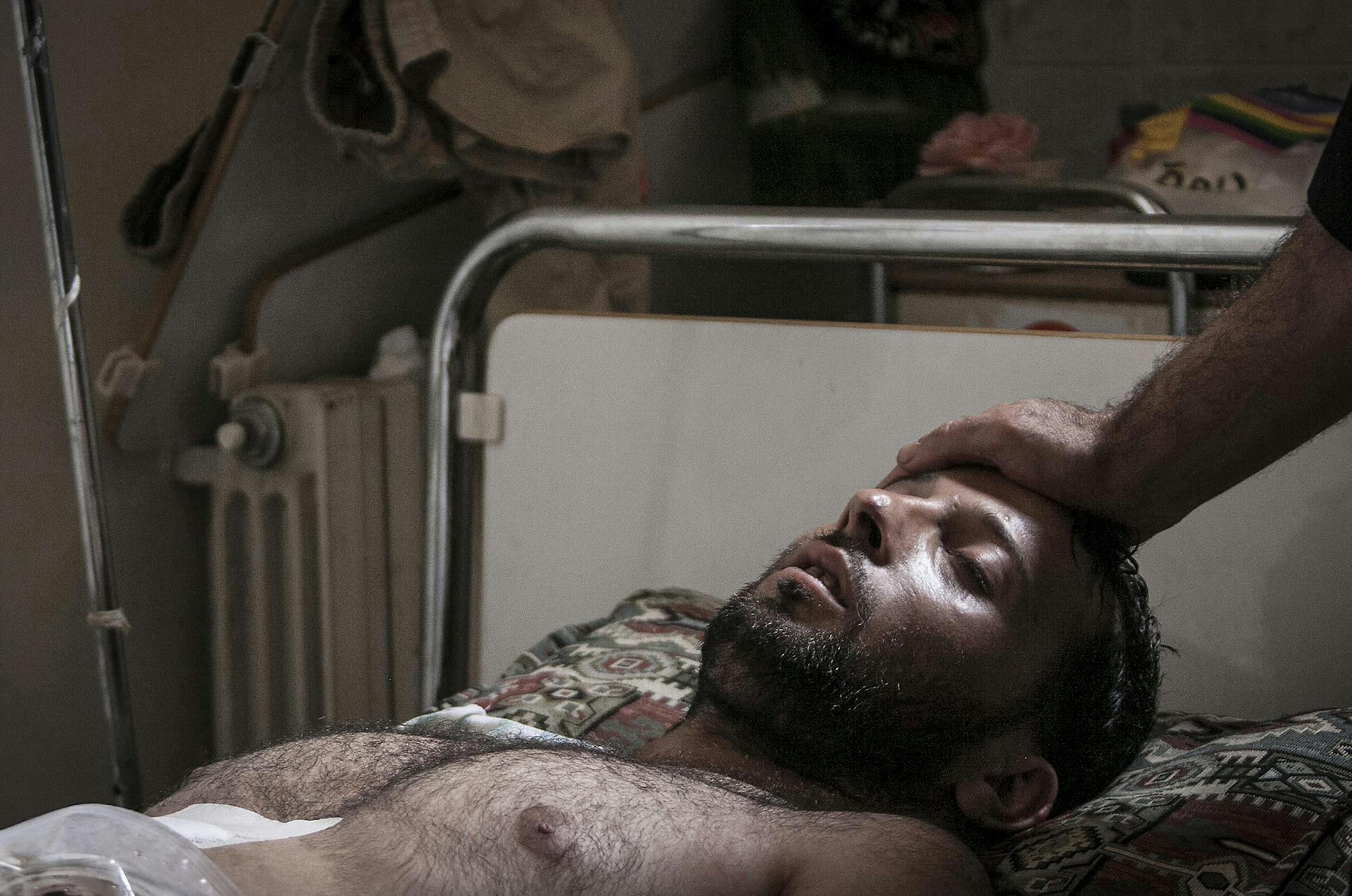 In this Sunday, Sept. 22, 2013 photo, a Syrian doctor touches the forehead of a wounded Free Syrian Army fighter laying on a bed at a field hospital in a village turned into a battlefield with government forces in Idlib province, northern Syria. (AP Photo) ORG XMIT: MIN2013102811530414