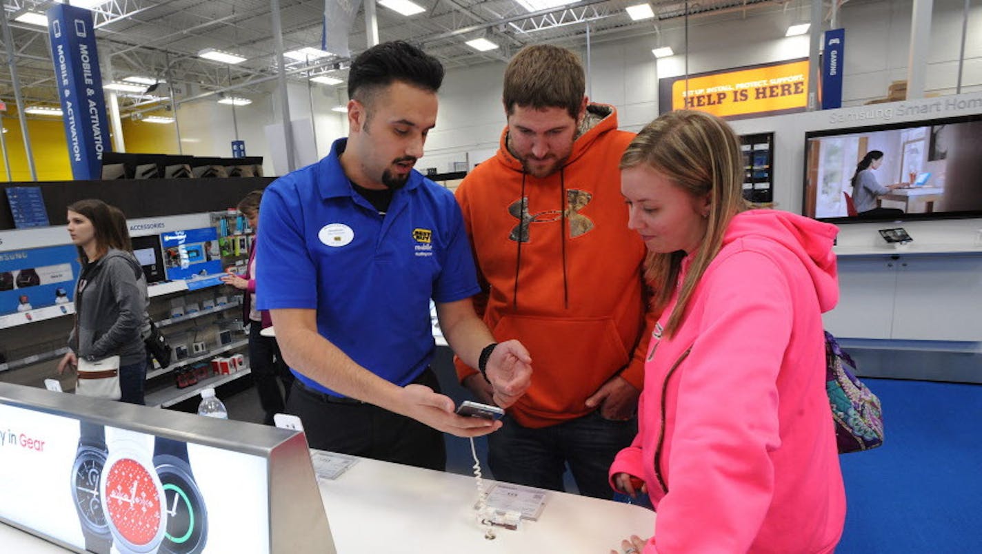 FILE - In this Friday, Nov. 27, 2015, file photo, Best Buy mobile associate Jonathan Maust, left, shows a smartphone to customers Brad Oaks and his wife, Nicole, of South Fork, Pa., in Johnstown, Pa. American businesses stepped up hiring in November, led by strong gains in retail, finance and other service industries, payroll processor ADP reported, Wednesday, Dec. 2, 2015. (John Rucosky/The Tribune-Democrat via AP, File)