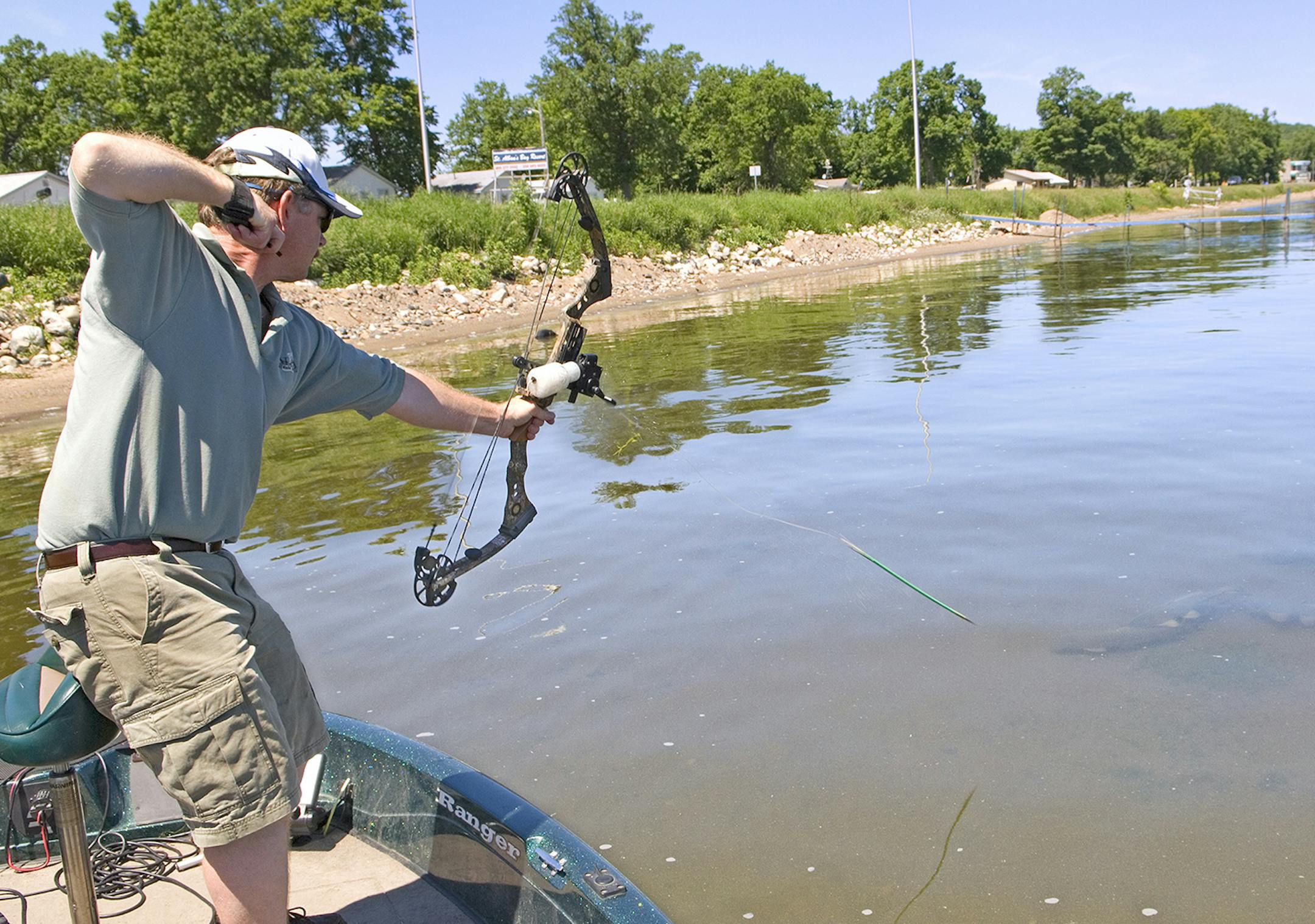 An bowfisherman releases an arrow at a group of three carp. Because of light refraction, he must aim low in order to hit his target.