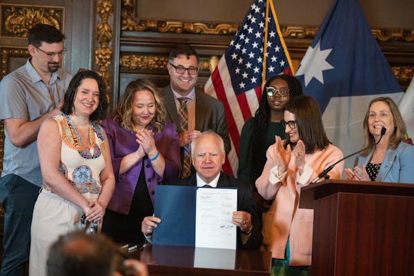 Gov. Tim Walz signs a bill preventing junk fees that was sponsored by Rep. Emma Greenman, seen left of the governor, and Sen. Lindsey Port, far left, 