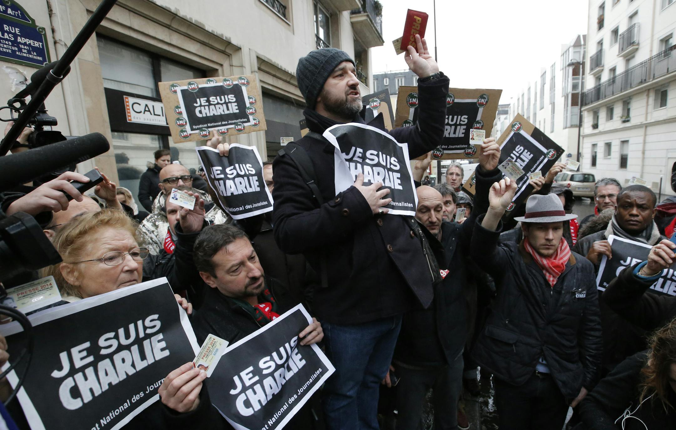Journalist hold up their press cards during a minute of silence outside the Charlie Hebdo newspaper in Paris, Thursday, Jan. 8, 2015, a day after masked gunmen stormed the offices of a satirical newspaper and killed 12 people. Protesters in some U.S. cities — repeating the viral online slogan "Je Suis Charlie" or "I Am Charlie"— demonstrated against the deadly terror attack on a Paris newspaper office, joining thousands around the world who took to the streets to rally against the
