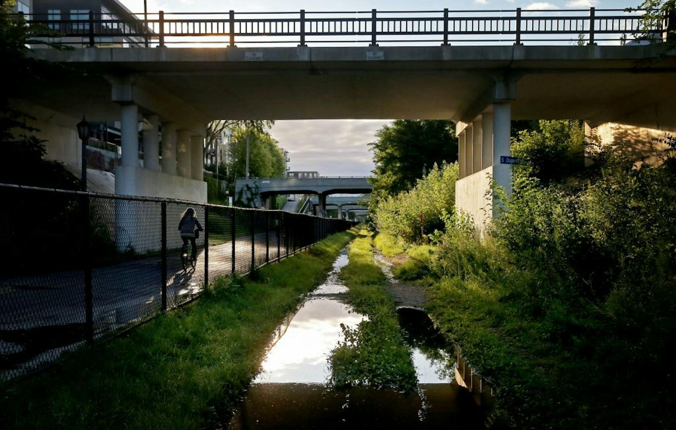 A bicyclist cruises along Midtown Greenway, beneath the Dupont Avenue bridge, near dawn as the sun paints the nearby bridges and vegetation with warm light Thursday, Aug. 20, 2015, along the Midtown Greenway in Minneapolis, MN. Underneath some of the nearby bridges live as many as 40 homeless people, according to an estimate by one of those homeless.