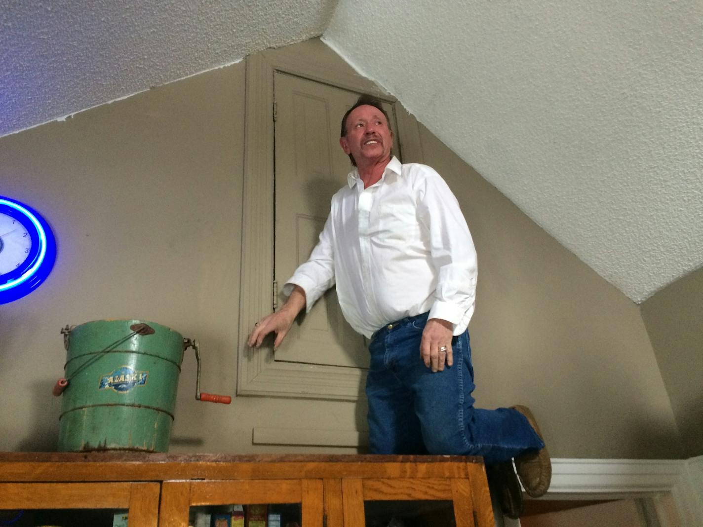 Arjo Adams climbs on a cabinet in his home to show how an attic access door is insulated, despite what a city code inspector found. The city of St. Paul wants to demolish the home, saying it's a safety hazard.