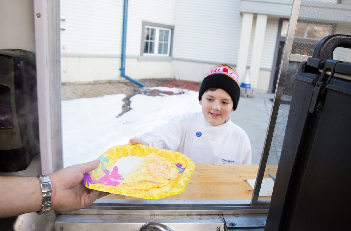Lucas Hobbs, 13, Founder of Chef Lucas Food, recieves a freshly prepared omelette by Kabomelette, a food truck, to deliever to residents at the Dakota