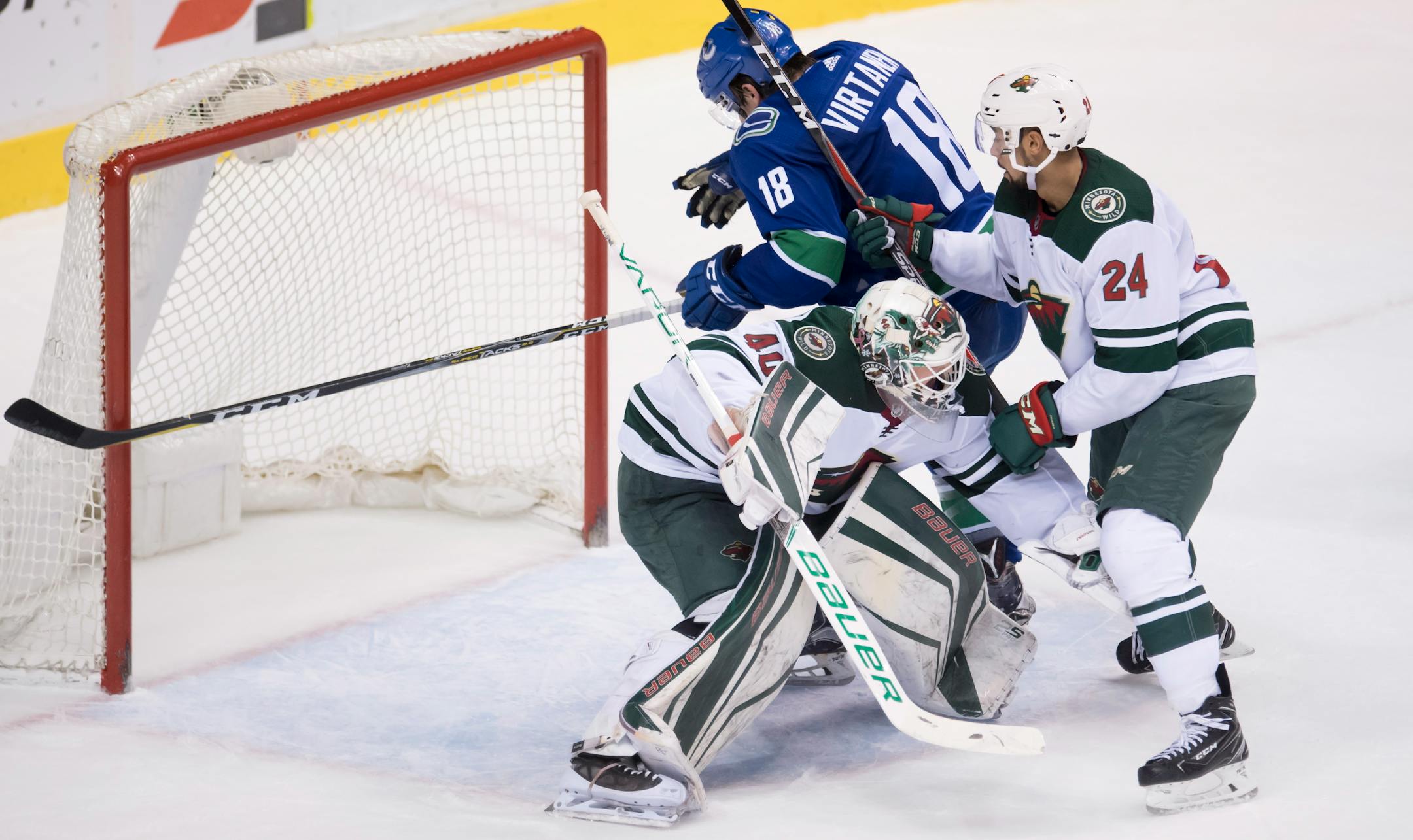 Minnesota Wild defenseman Matt Dumba (24) tries to clear Vancouver Canucks right wing Jake Virtanen (18) from Wild goaltender Devan Dubnyk (40) during the third period of an NHL hockey game Friday, March 9, 2018, in Vancouver, British Columbia. (Jonathan Hayward/The Canadian Press via AP)