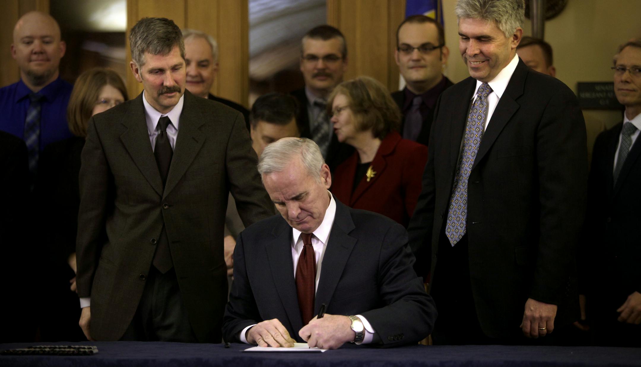 Senator Tony Lourey (left of Dayton) and Representative Joe Atkins (right of Dayton) watched as Governor Mark Dayton, flanked by 40 state lawmakers, signed the Minnesota Health Insurance Exhange Bill into law at the Capitol in St. Paul on March 20, 2013.