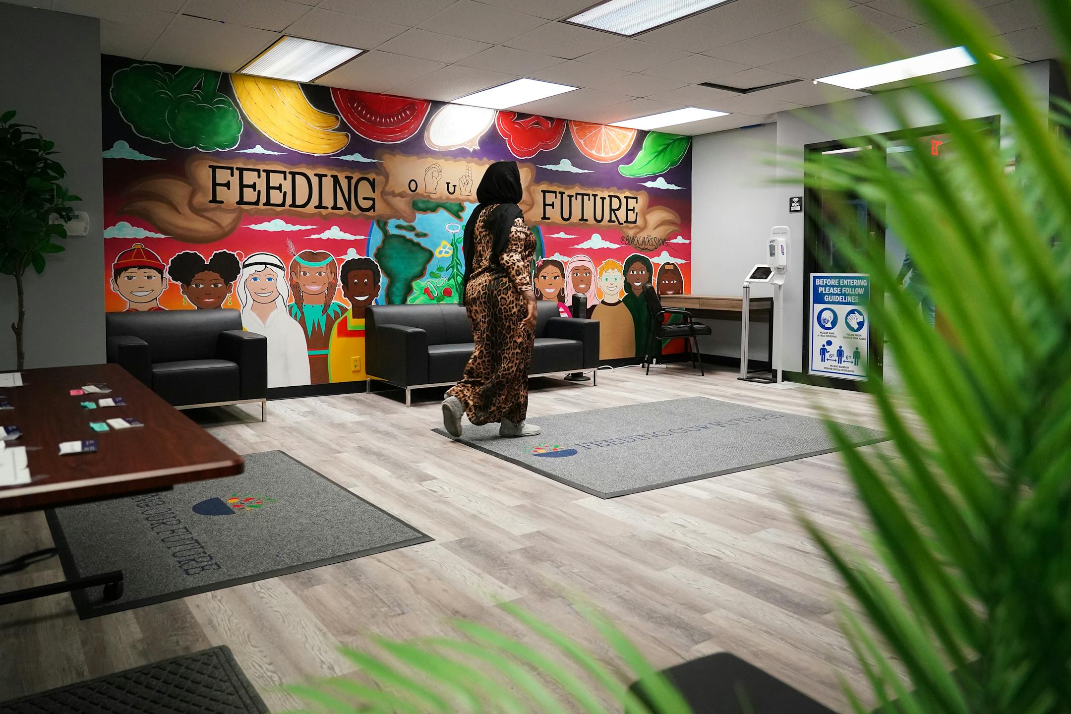 Woman in leopard print dress walks through office with colorful Feeding Our Future mural on wall.