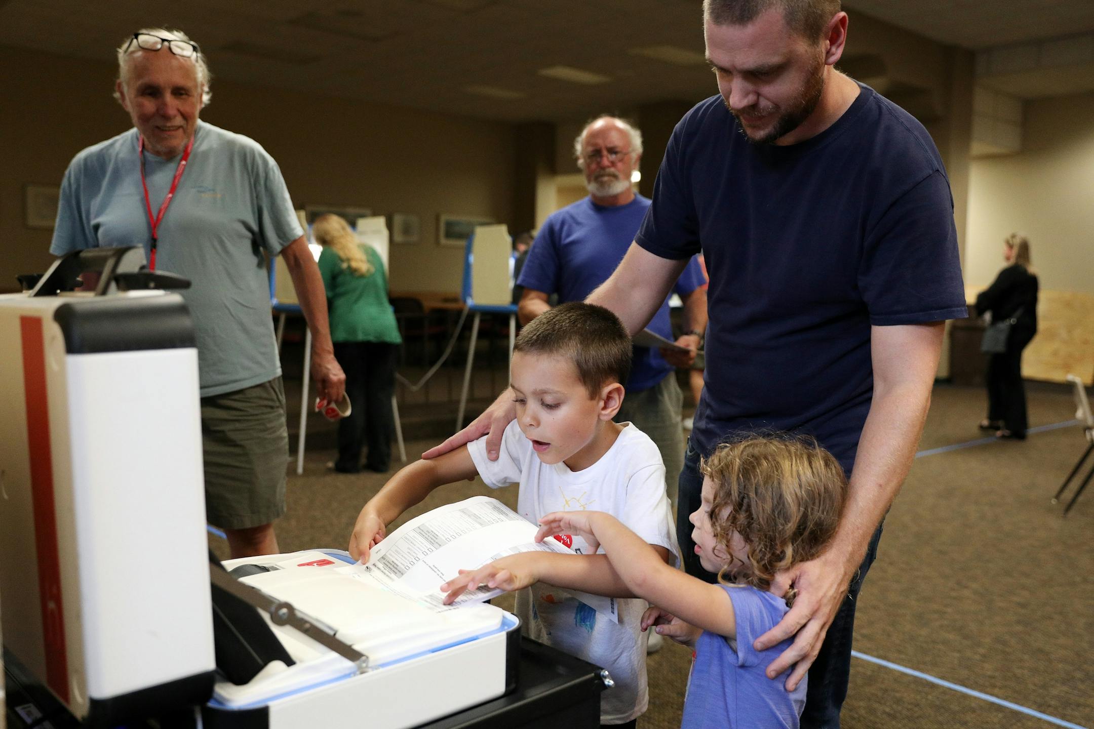 Tyson Reed got some help casting his ballot from his son Leif, 5, and daughter Siena, 3, as election judge James McKenzie looked on at Holy Spirit Catholic Church in St. Paul. To be official Reed pushed the ballot into the machine himself.
