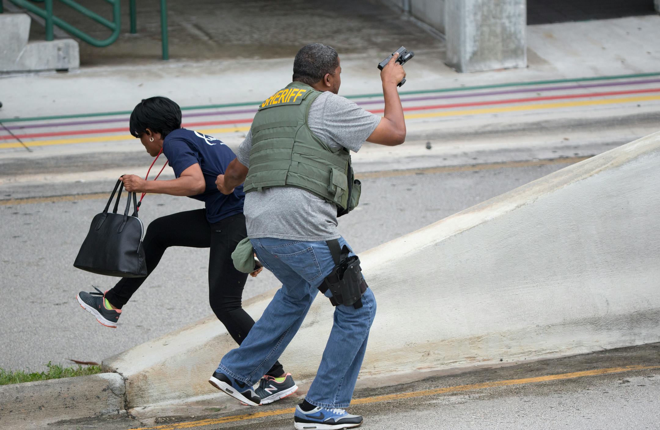 A law enforcement officer evacuates a civilian from an area at Fort Lauderdale-Hollywood International Airport, Friday, Jan. 6, 2017, in Fort Lauderdale, Fla. A gunman opened fire in the baggage claim area at the airport Friday, killing several people and wounding others before being taken into custody in an attack that sent panicked passengers running out of the terminal and onto the tarmac, authorities said. (AP Photo/Wilfredo Lee)