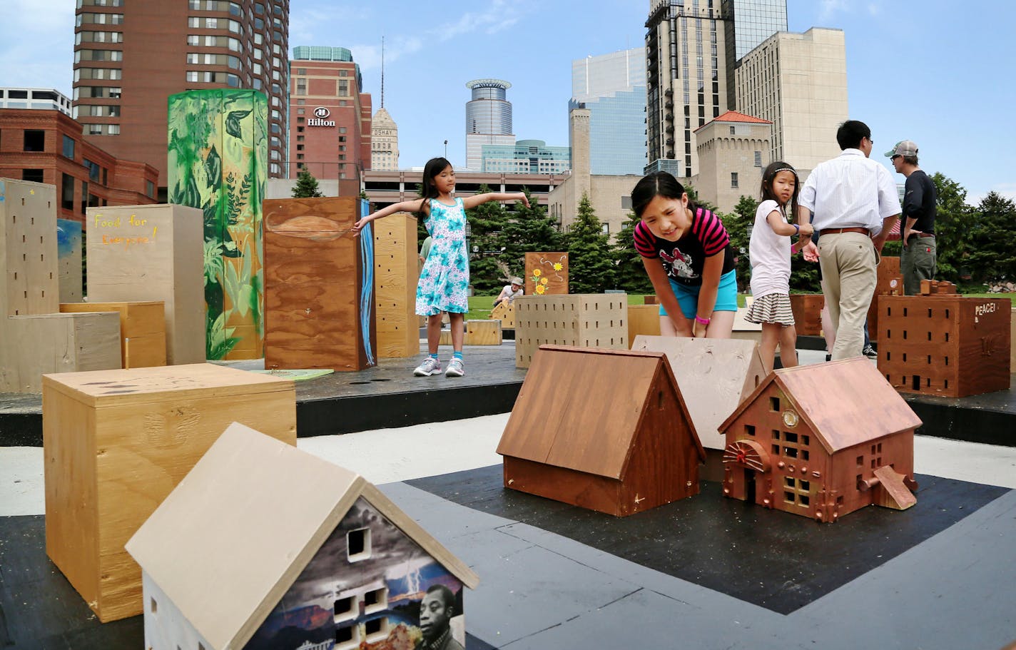 Mini_Polis is a miniature model of Minneapolis, built in collaboration with many people who live here and in Minnesota or have connections to Minneapolis. Here, Sisters Alice Hue, 7, of Rochester, MN, left to right, and Ellen Hue, 9, and their friend Gracie Quang, 8, with her dad Bo, helped paint a house for the project and had just picked out a spot for their house. The model city is on display at the Minneapolis Convention Center Plaza and was seen Saturday, June 6, 2015, in Minneapolis, MN.](