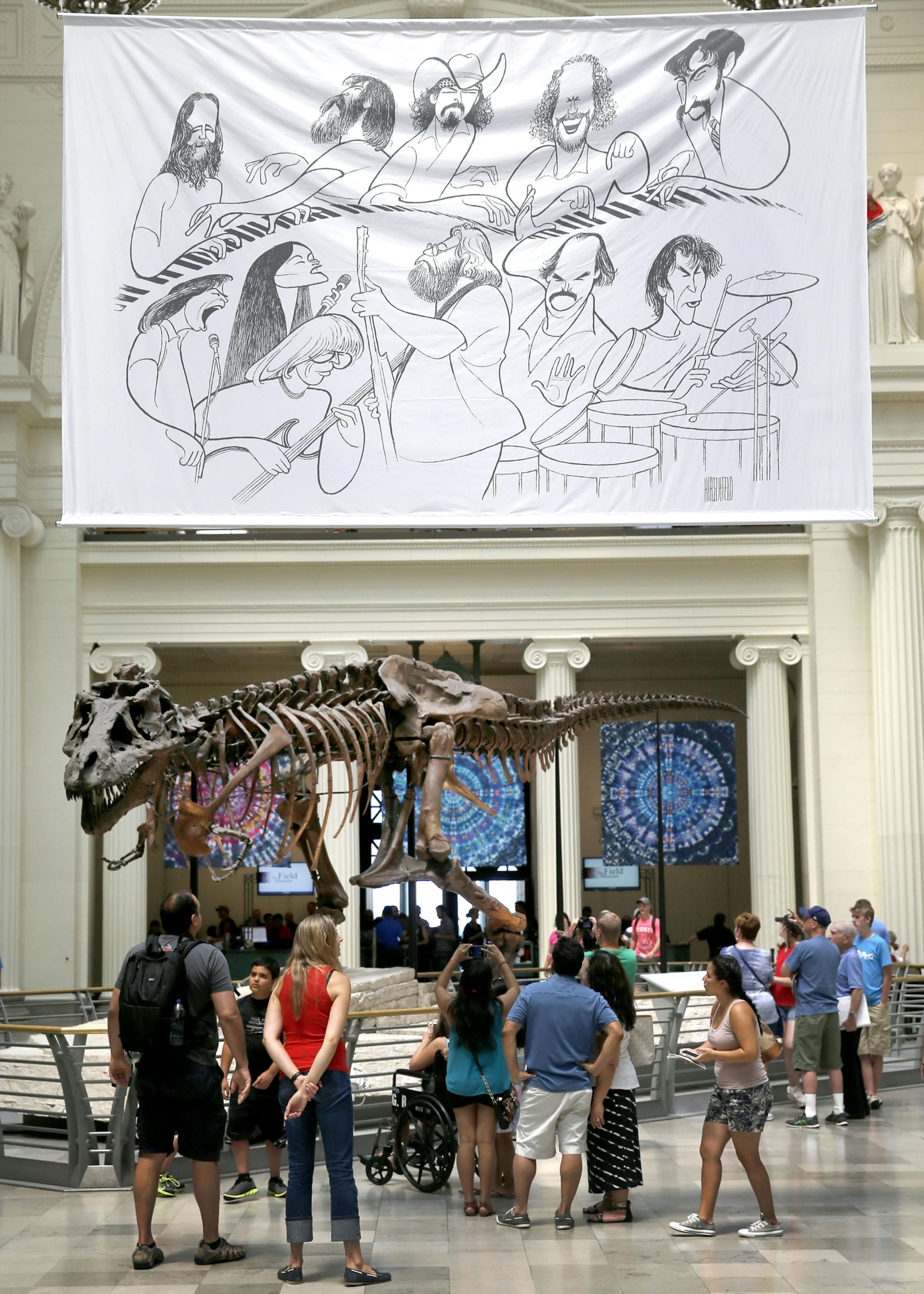 In this photo taken Tuesday, June 30, 2015, a banner of an Al Hirschfeld caricature of the Grateful Band members hangs over the Field Museum's famous Sue, the most extensive Tyrannosaurus rex specimen ever found, as part of a Dead exhibit in Chicago. The Dead will perform over the July 4th weekend at Soldier Field. (AP Photo/Charles Rex Arbogast)