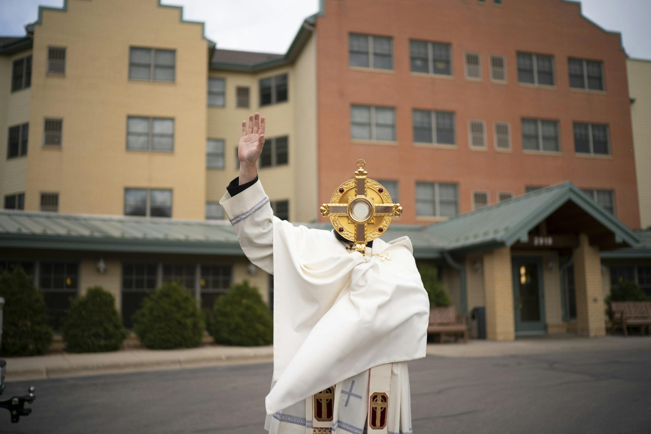 Fr. Spencer Howe, Pastor at Holy Cross Catholic Church, waved to a parishioner's mother inside RiverVillage North, a Catholic Eldercare residence for seniors in Northeast Minneapolis.