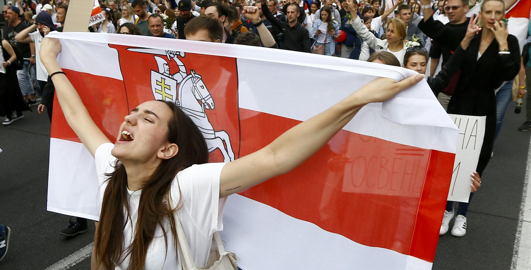 A woman reacts as she marches holding an old Belarusian national flag in the center of Minsk, Belarus, Friday, Aug. 14, 2020. Some thousands of people have flooded the cnetre of the Belarus capital, Minsk, in a show of anger over a brutal police crackdown this week on peaceful protesters that followed a disputed election. (AP Photo/Sergei Grits)