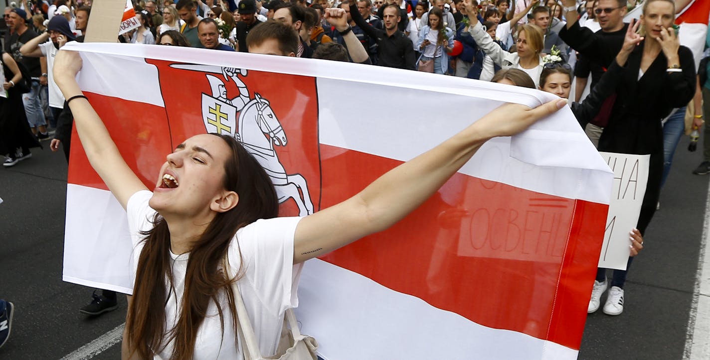 A woman reacts as she marches holding an old Belarusian national flag in the center of Minsk, Belarus, Friday, Aug. 14, 2020. Some thousands of people have flooded the cnetre of the Belarus capital, Minsk, in a show of anger over a brutal police crackdown this week on peaceful protesters that followed a disputed election. (AP Photo/Sergei Grits)