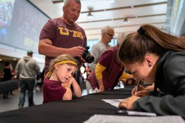 Alayna Sandbulte, 5, watched as Anne Miller signed her photo on the team roster. Her dad Craig stood behind her. The Gophers softball team has a rally