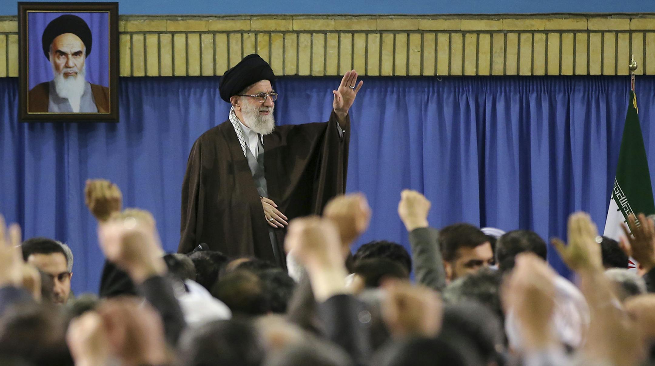 In this picture released by an official website of the office of the Iranian supreme leader, Supreme Leader Ayatollah Ali Khamenei waves while attending a meeting with a group of environmental officials and activists at his residence in Tehran, Iran, Sunday, March, 2015. A portrait of the late revolutionary founder Ayatollah Khomeini hangs in background. (AP Photo/Office of the Iranian Supreme Leader)
