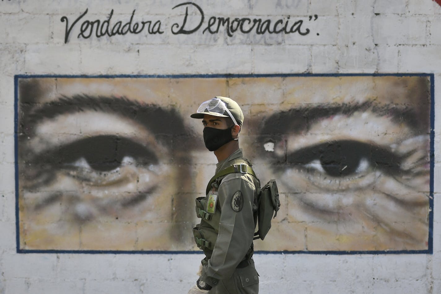 A soldier guards a voting poll at a school that has the eyes of the late President Hugo Chavez painted on a wall during elections to choose members of the National Assembly in Caracas, Venezuela, Sunday, Dec. 6, 2020. The vote, championed by President Nicolas Maduro, is rejected as fraud by the nation's most influential opposition politicians.